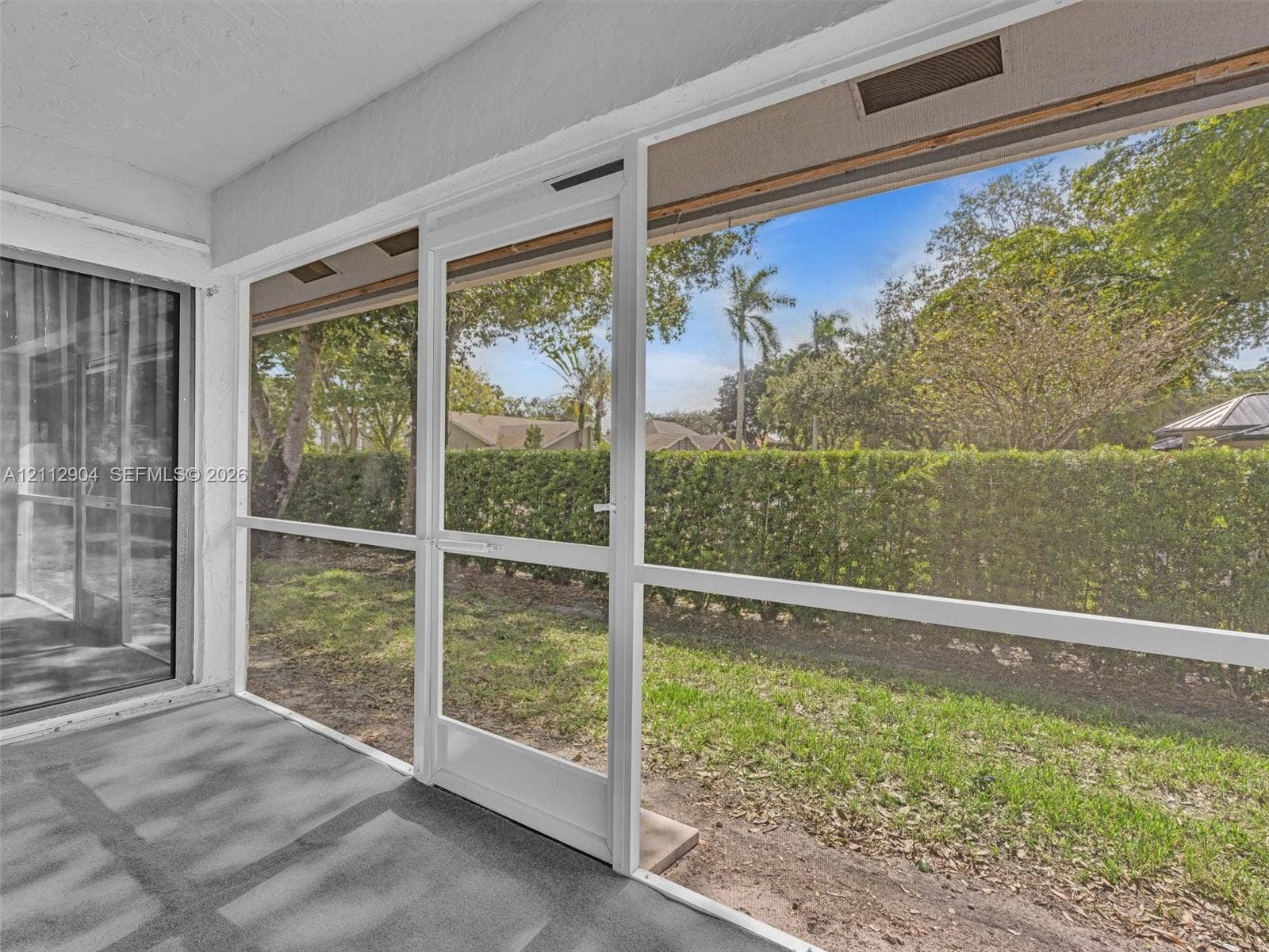 76 Forest Circle, Cooper City, FL 33026 Screened-in porch featuring a concrete floor, white aluminum framing, and a screen door, opening to a grass yard with a perimeter privacy hedge