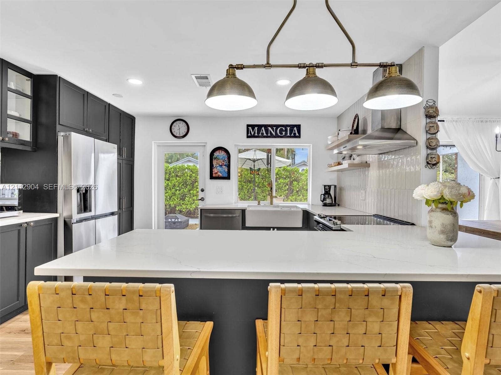76 Forest Circle, Cooper City, FL 33026 Kitchen featuring dark cabinetry, quartz countertops, a farmhouse-style sink, stainless steel range hood, and a multi-light pendant fixture