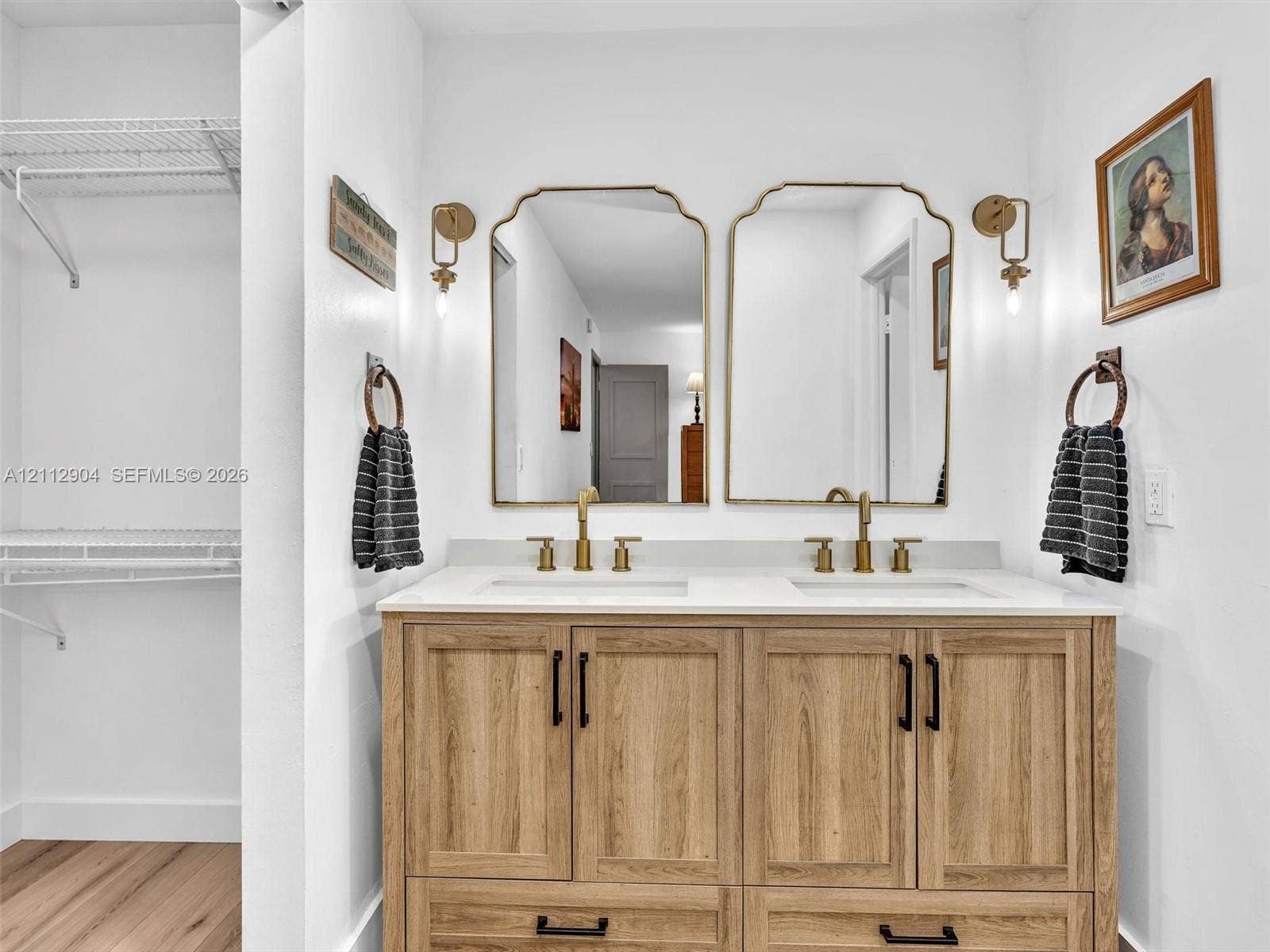 76 Forest Circle, Cooper City, FL 33026 Double vanity featuring wood-finish cabinetry, solid surface countertop with integrated dual sinks, metallic finish faucets, and arched wall mirrors with wall-mounted light fixtures