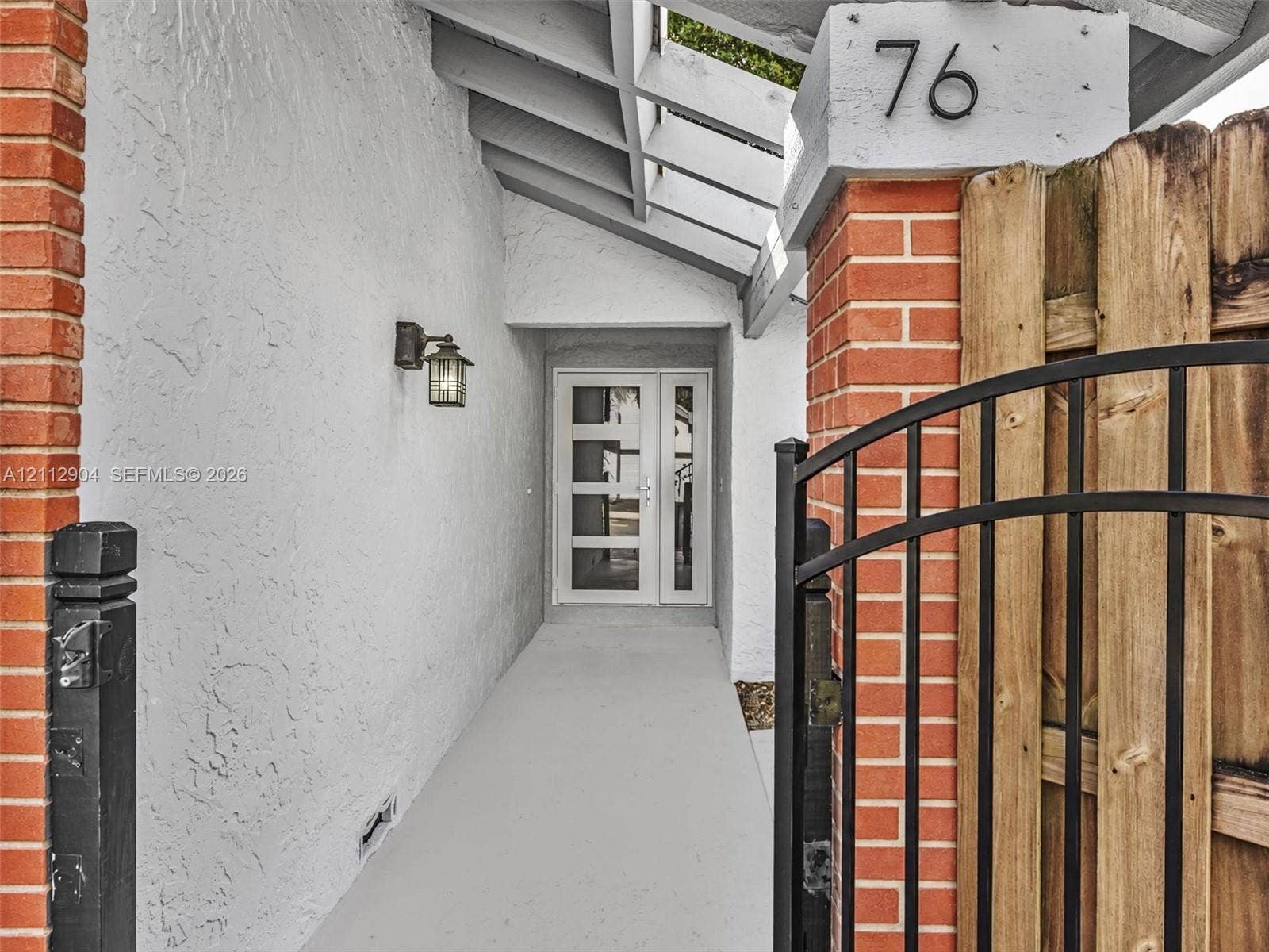 76 Forest Circle, Cooper City, FL 33026 Covered entryway featuring a brick-accented stucco facade, open-beam ceiling, metal gate, and a multi-panel glass-inset entry door