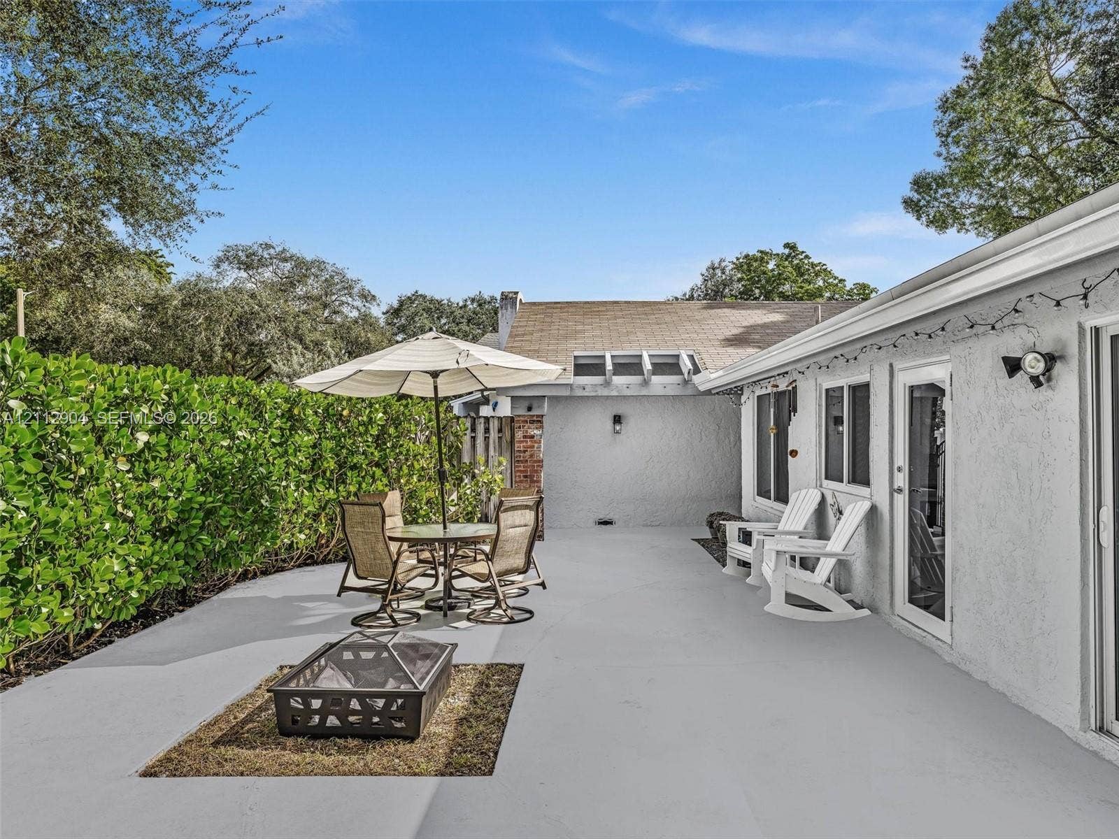 76 Forest Circle, Cooper City, FL 33026 Expansive concrete patio featuring a dedicated fire pit area, stucco exterior, and tall privacy hedging