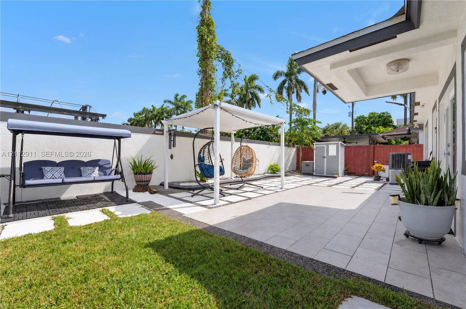 217 SW 15th Place, Homestead, FL 33030 Backyard featuring a paved patio with geometric stone inlay, a covered pergola structure, a solid perimeter wall, and a maintained lawn area