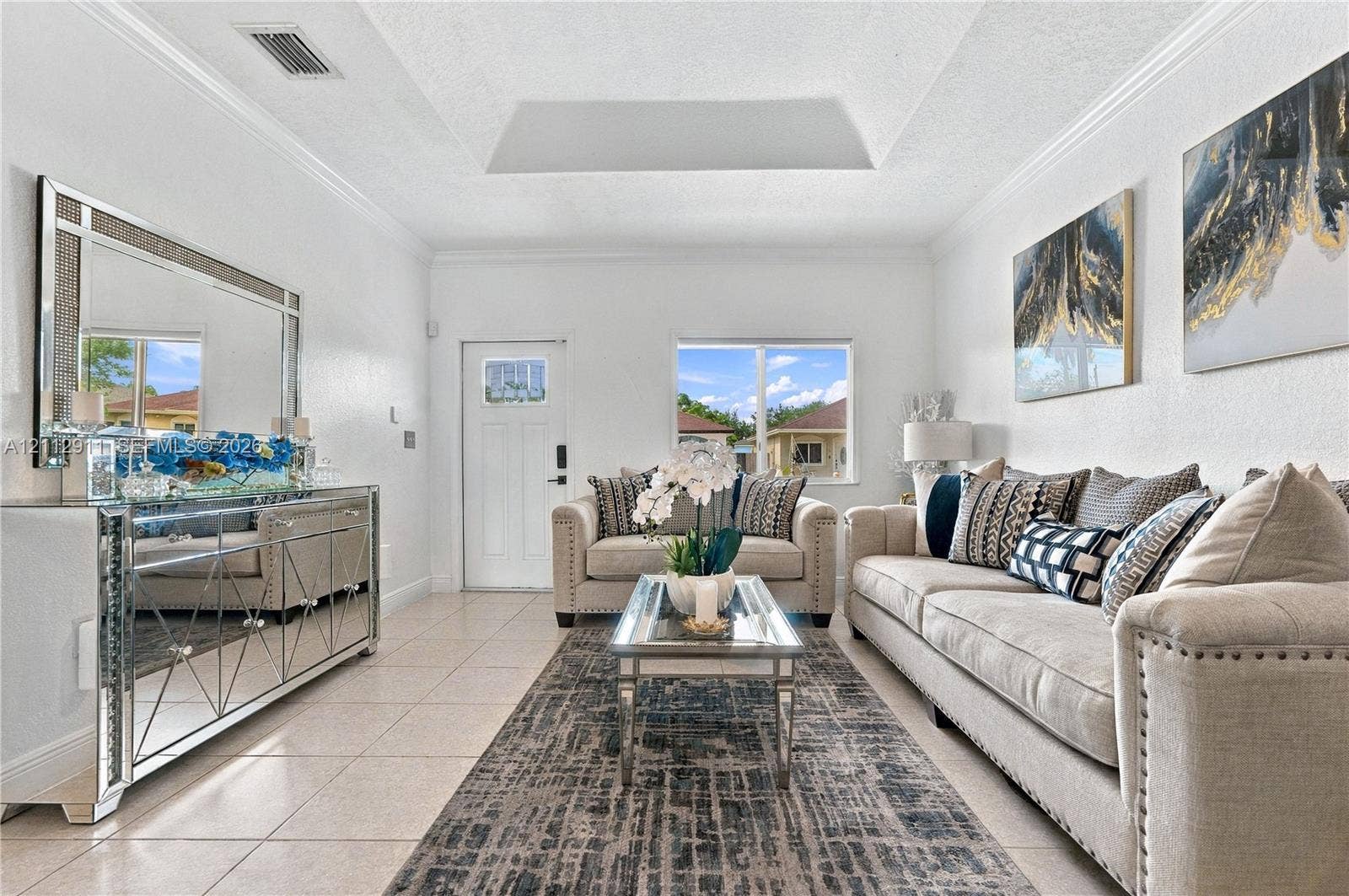 217 SW 15th Place, Homestead, FL 33030 Living area featuring a tray ceiling, crown molding, neutral tile flooring, and a single-light entry door