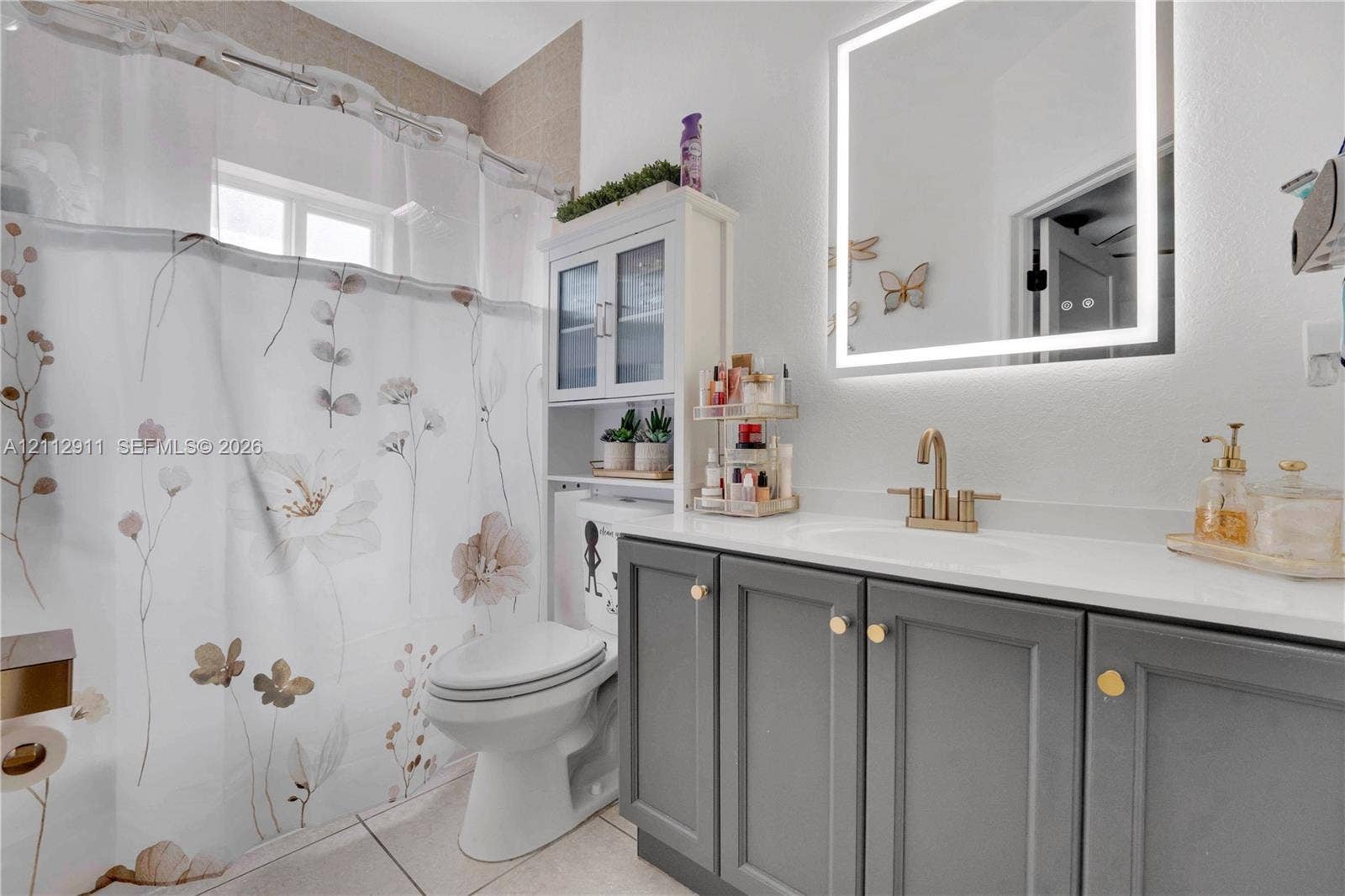 217 SW 15th Place, Homestead, FL 33030 Bathroom featuring a gray shaker-style vanity with a solid-surface countertop, an integrated sink with a brass-finish faucet, and a wall-mounted LED-backlit mirror