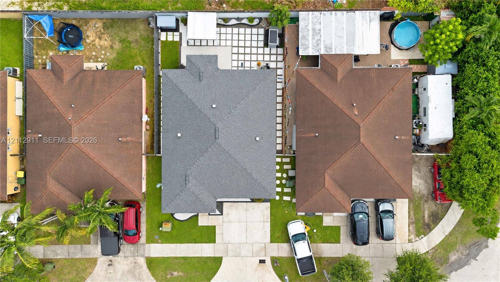 217 SW 15th Place, Homestead, FL 33030 Aerial perspective featuring a central residential property with a multi-hipped shingle roof, a concrete driveway, a front lawn, and a rear patio area composed of large-format pavers