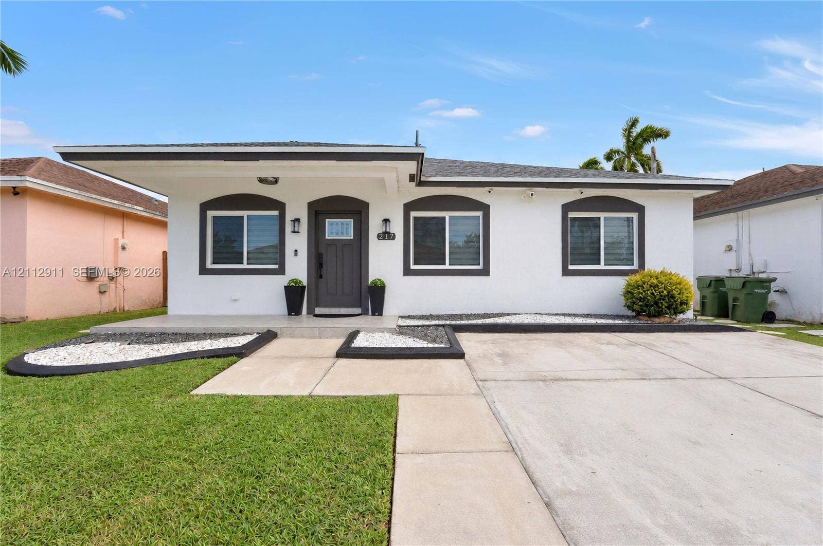 217 SW 15th Place, Homestead, FL 33030 Single-story exterior featuring a covered front porch, arched window trim, concrete driveway, and minimalist landscape design with stone-accented beds