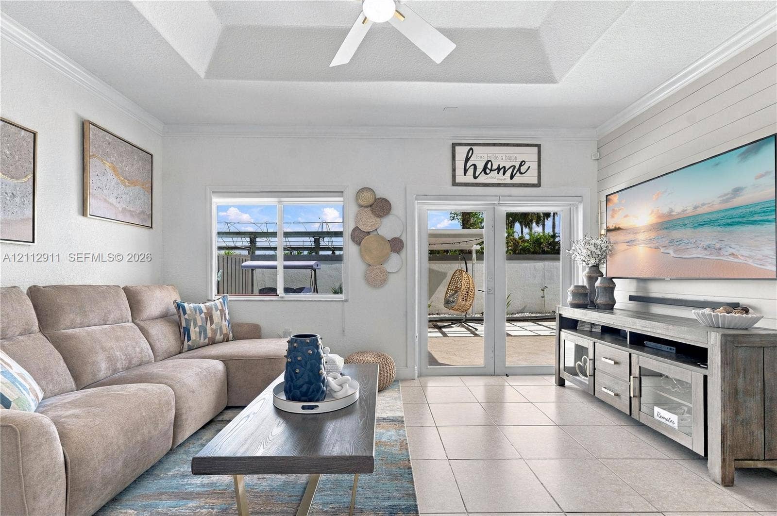 217 SW 15th Place, Homestead, FL 33030 Living area featuring a tray ceiling with a recessed ceiling fan, horizontal shiplap wall accent, tile flooring, and double glass doors providing exterior access