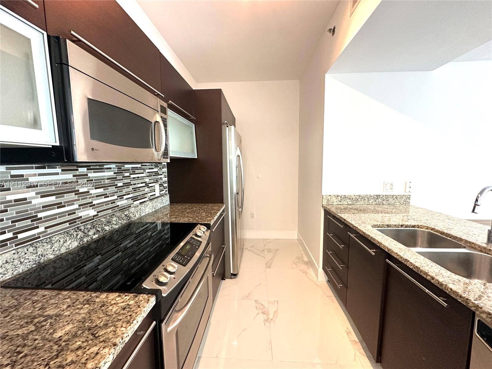 951 Brickell Avenue, #2601, Miami, Miami, FL 33131 Kitchen featuring dark wood-finish cabinetry, stainless steel appliances, speckled stone countertops, mosaic tile backsplash, and light-toned tile flooring