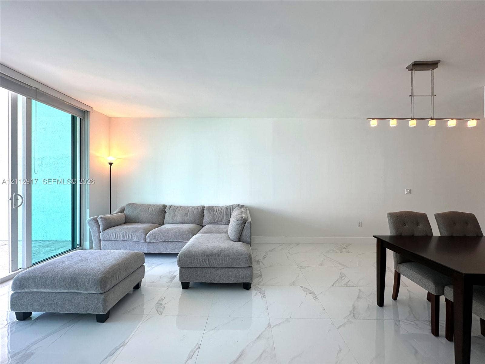 951 Brickell Avenue, #2601, Miami, Miami, FL 33131 Large-format polished tile flooring featuring a vein-patterned finish, full-height sliding glass doors, and a linear multi-light pendant fixture with a brushed metal finish