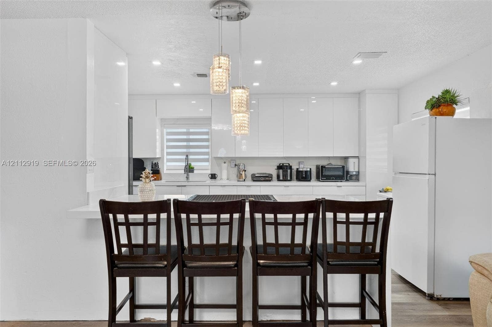 2120 NW 28th Terrace, Fort Lauderdale, FL 33311 Kitchen featuring high-gloss white cabinetry, white countertops, a multi-tier crystal pendant light fixture, recessed lighting, and a breakfast bar