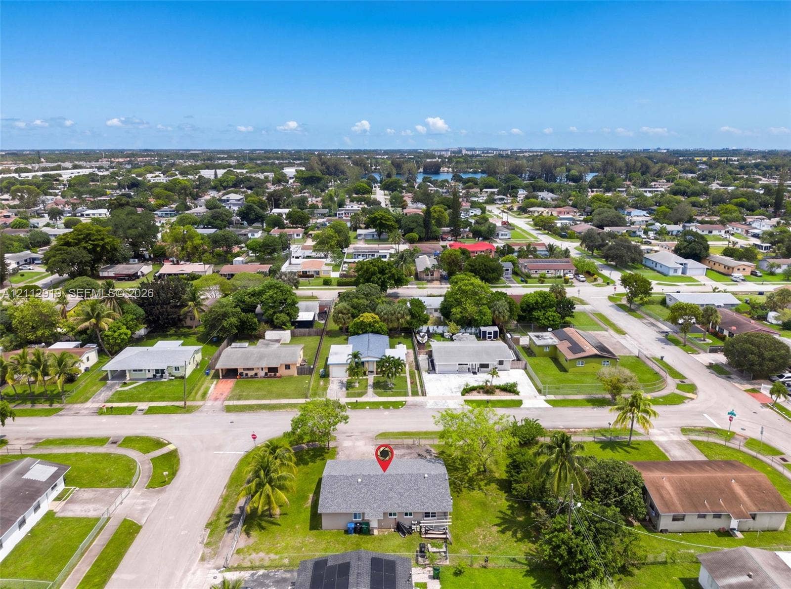 2120 NW 28th Terrace, Fort Lauderdale, FL 33311 Aerial perspective of a corner lot residence featuring a pitched shingle roof, expansive grass lawn, and mature palm trees