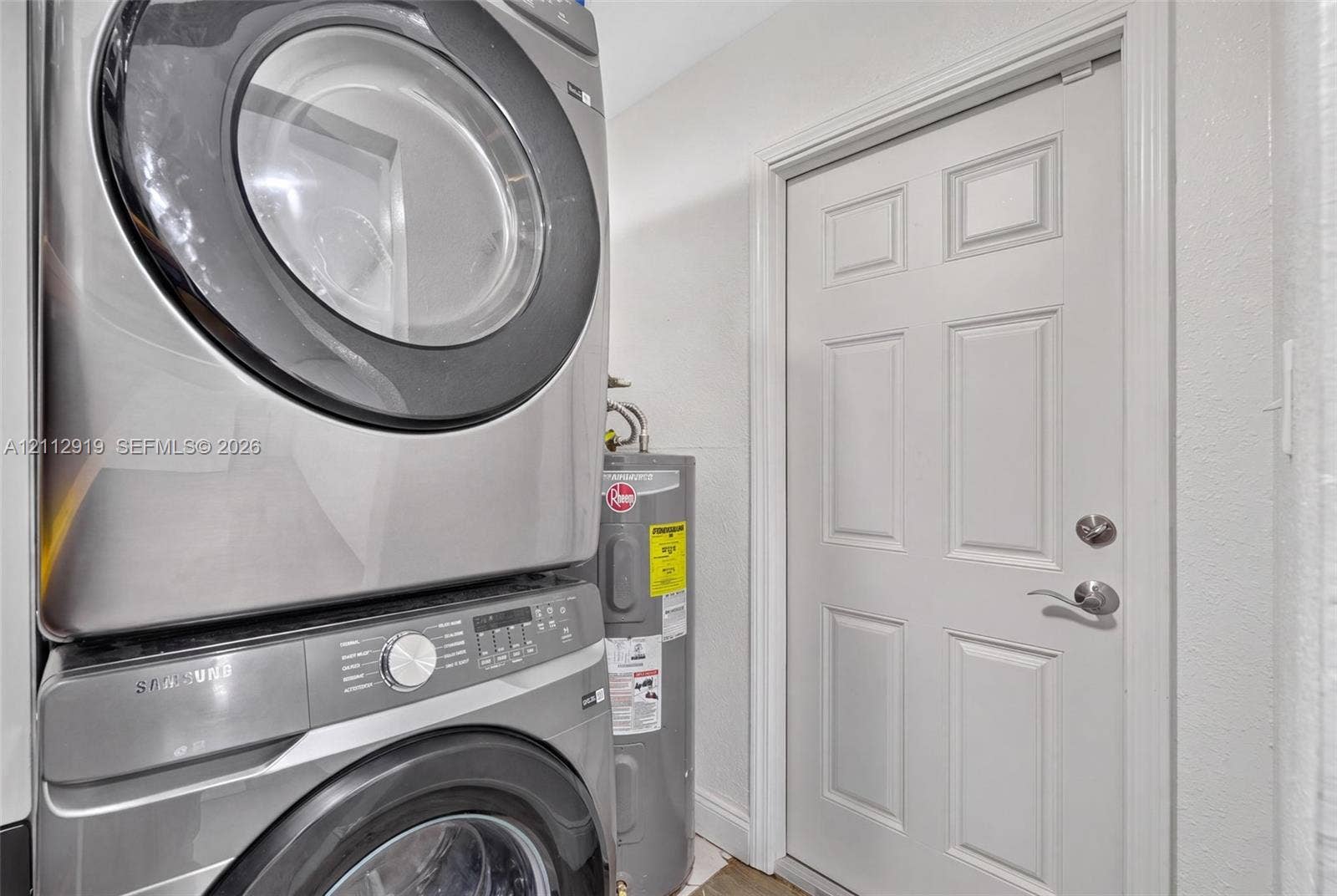 2120 NW 28th Terrace, Fort Lauderdale, FL 33311 Stacked stainless steel front-load laundry appliances and a vertical water heater paired with a six-panel interior door featuring satin nickel hardware
