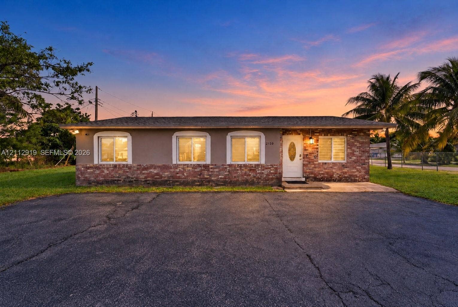 2120 NW 28th Terrace, Fort Lauderdale, FL 33311 Single-story exterior featuring a brick facade base, stucco upper walls, arched window trim, and a paved asphalt driveway