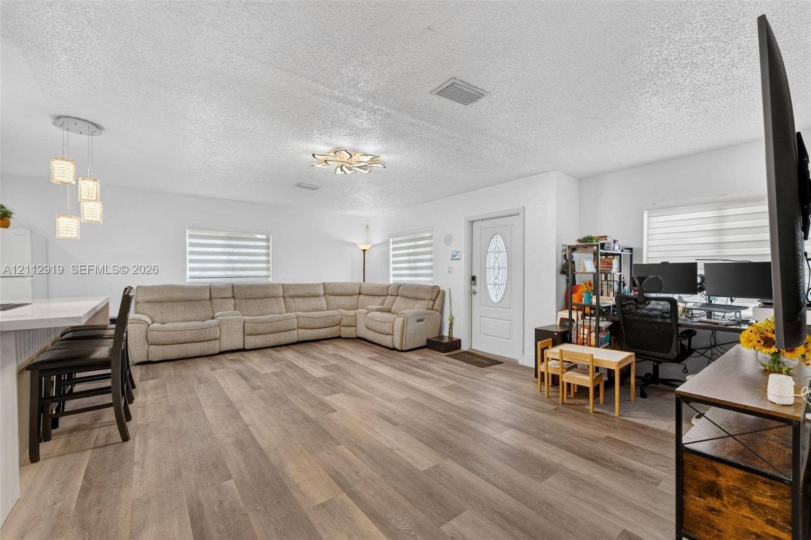 2120 NW 28th Terrace, Fort Lauderdale, FL 33311 Open-concept space featuring wood-finish flooring, multi-light pendant fixtures, tiered flush-mount ceiling lighting, and windows with integrated horizontal blinds