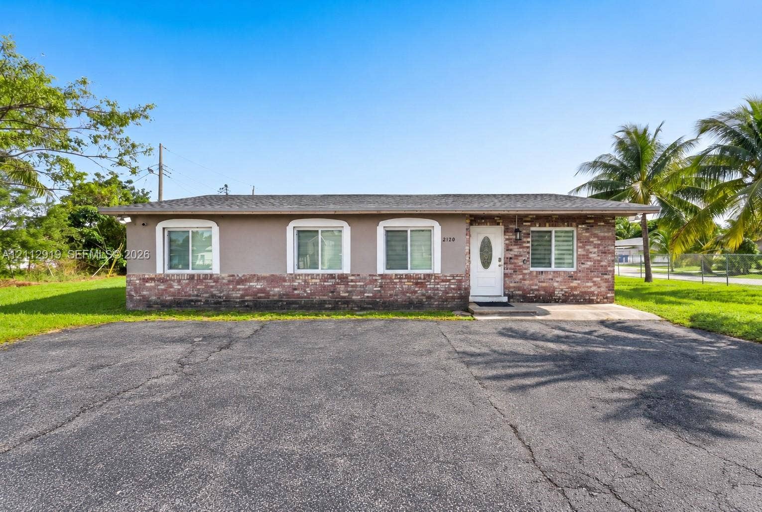 2120 NW 28th Terrace, Fort Lauderdale, FL 33311 Single-story exterior featuring a brick masonry lower facade, stucco upper walls, white-trimmed windows, a shingled roof, and an asphalt driveway