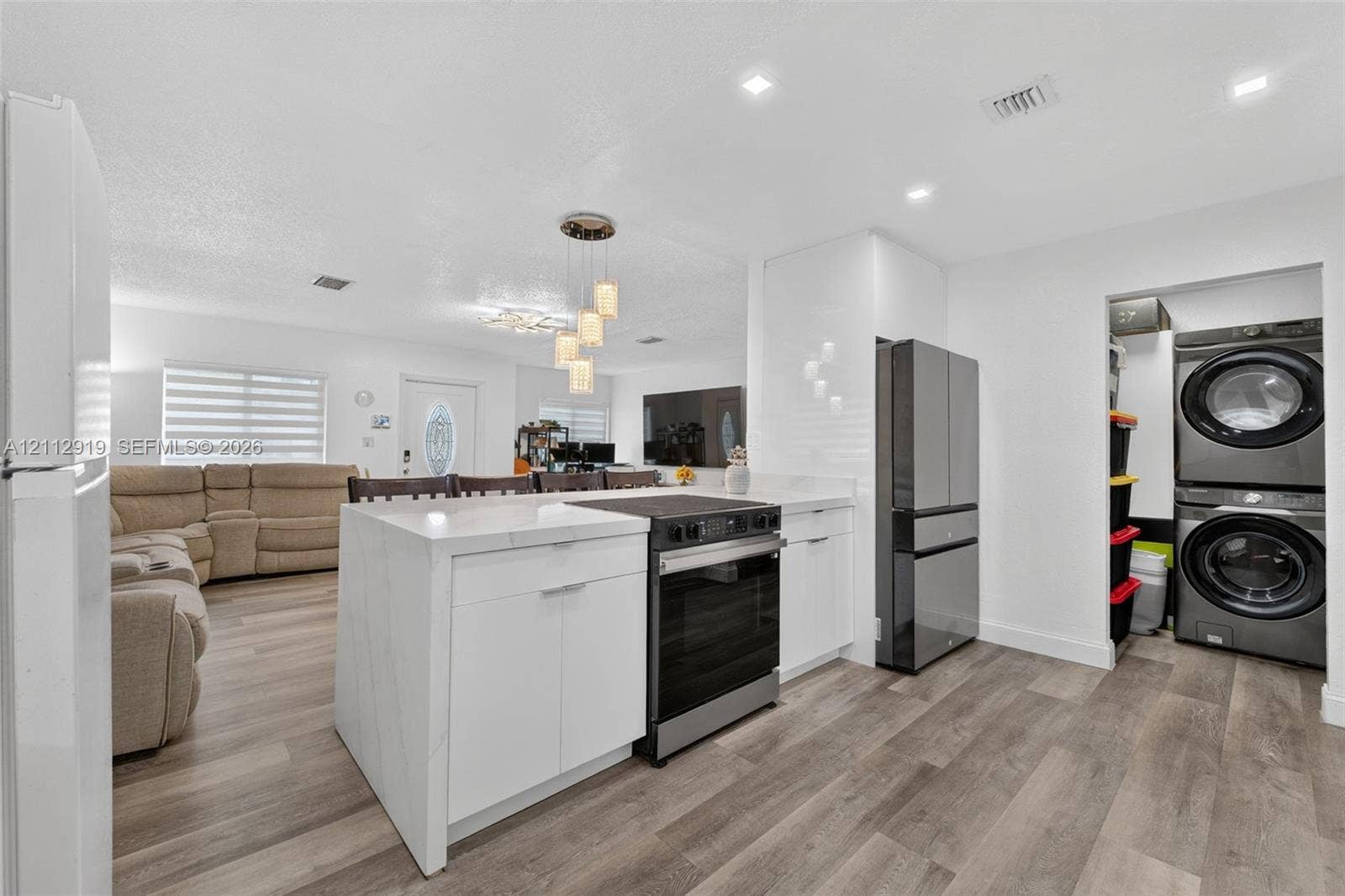 2120 NW 28th Terrace, Fort Lauderdale, FL 33311 Kitchen island featuring a stone countertop, wood-finish flooring, recessed lighting, and a dedicated laundry area with stacked washer and dryer unit