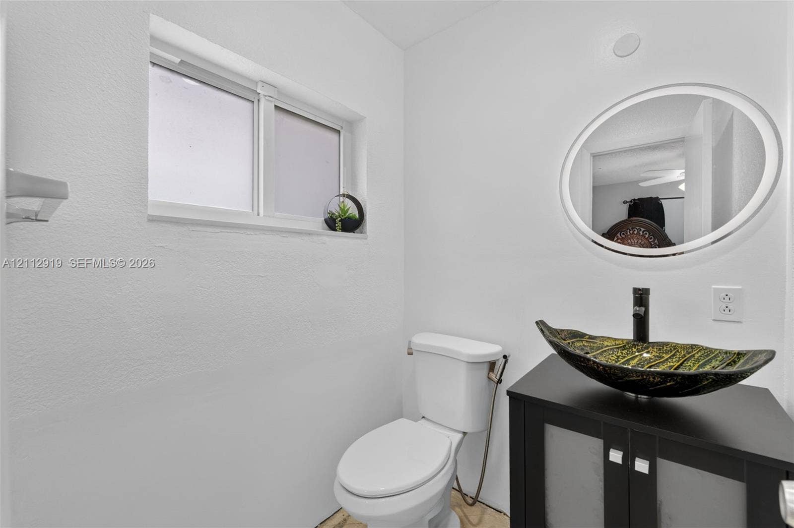 2120 NW 28th Terrace, Fort Lauderdale, FL 33311 Bathroom featuring a dark wood-finish vanity, decorative vessel sink, black faucet, oval wall mirror, and sliding window
