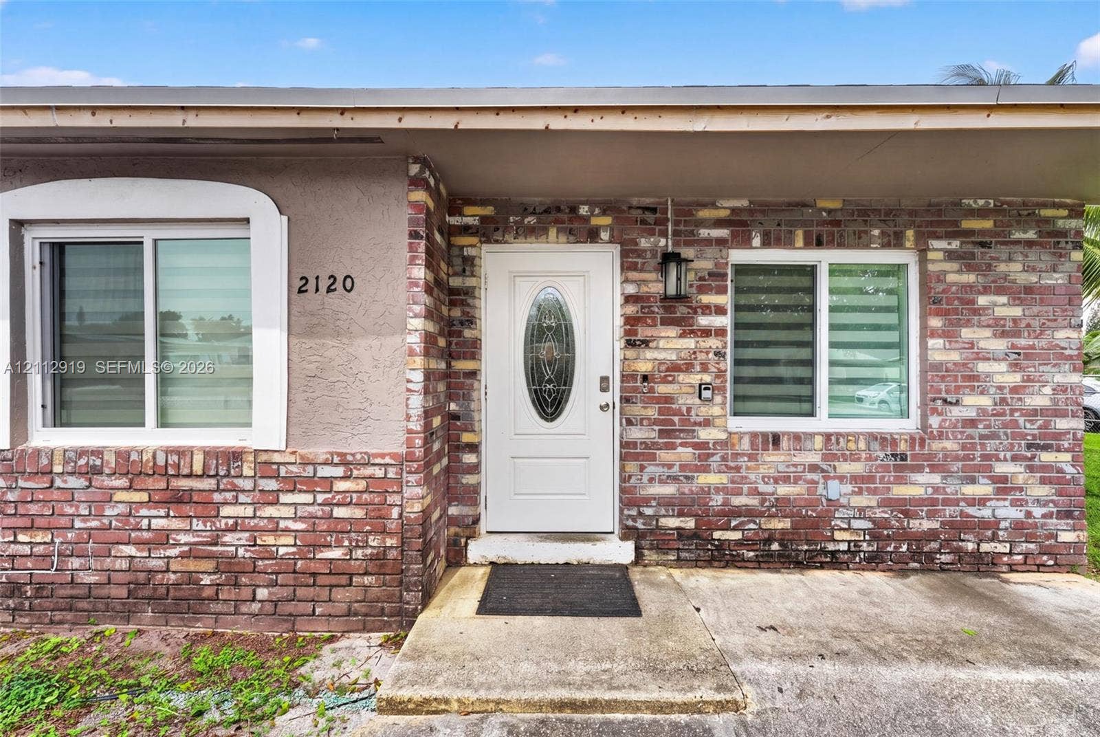 2120 NW 28th Terrace, Fort Lauderdale, FL 33311 Exterior facade featuring multi-tone brick masonry, smooth-finish stucco, a white entry door with an oval glass insert, and sliding windows