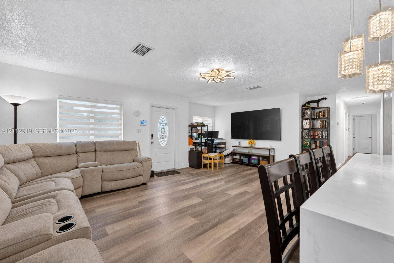 2120 NW 28th Terrace, Fort Lauderdale, FL 33311 Open-concept interior featuring wood-finish flooring, multi-light pendant fixtures, a modern floral-inspired ceiling light, and an exterior door with decorative glass insert