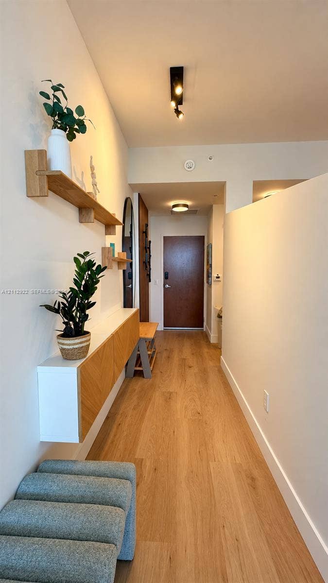Entryway featuring wood-finish flooring, a wall-mounted floating storage console with herringbone-patterned cabinet doors, multi-level wood shelving, and directional track lighting
