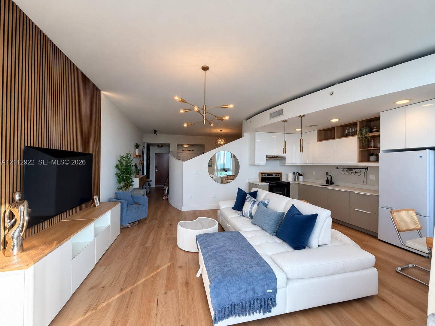 Wood-slat accent wall, integrated cabinetry, wood-finish flooring, multi-arm chandelier, and contemporary circular wall cutout