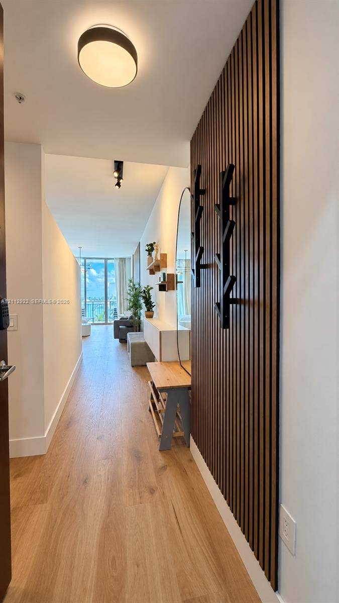Entryway featuring wood-finish flooring, a floor-to-ceiling slatted wood wall panel, matte black wall-mounted hooks, and contemporary disc-style ceiling lighting
