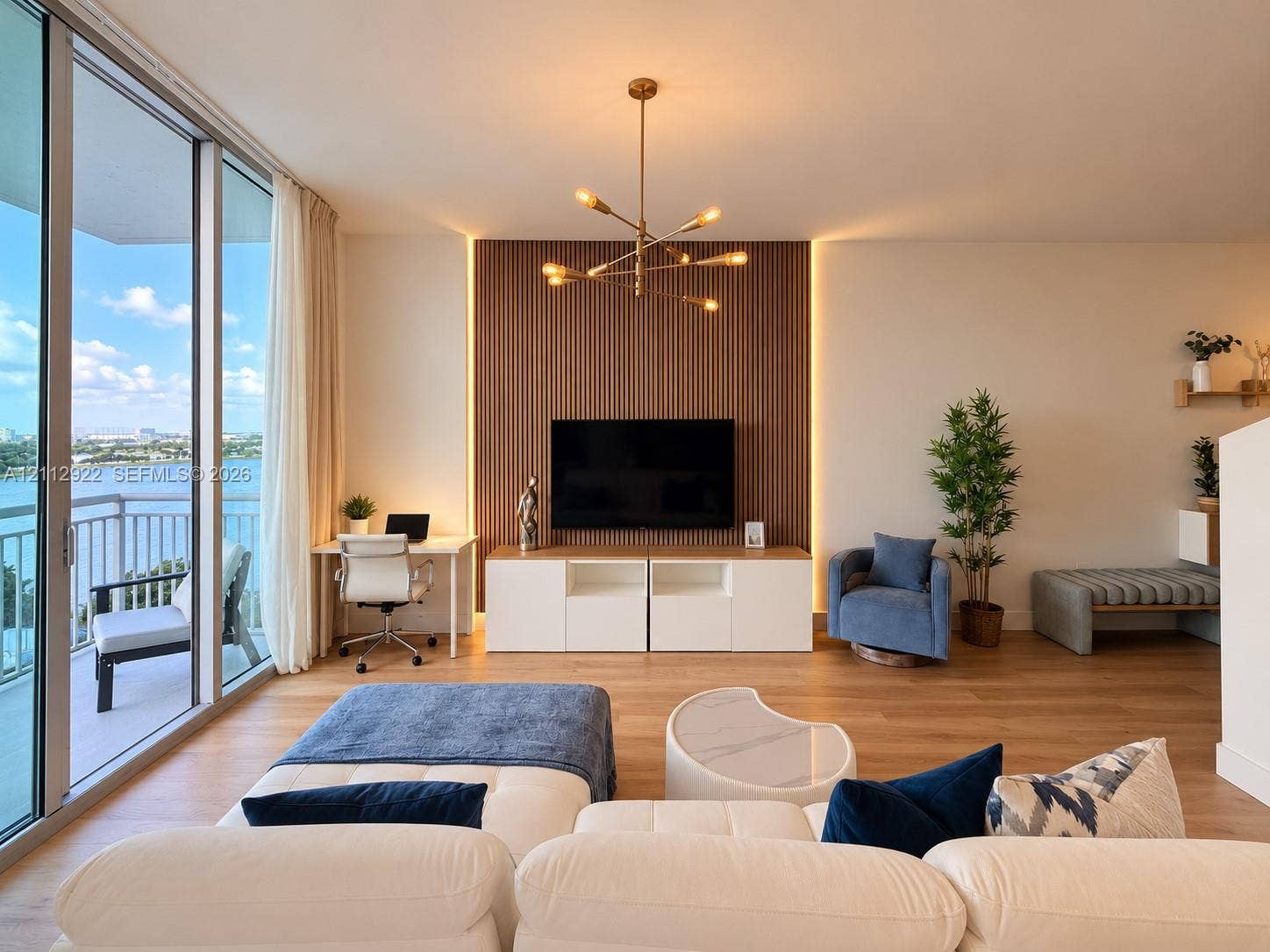 Living area featuring floor-to-ceiling glass sliding doors, wood-finish flooring, floor-to-ceiling vertical wood slat accent wall with perimeter integrated lighting, contemporary multi-arm chandelier, and covered balcony