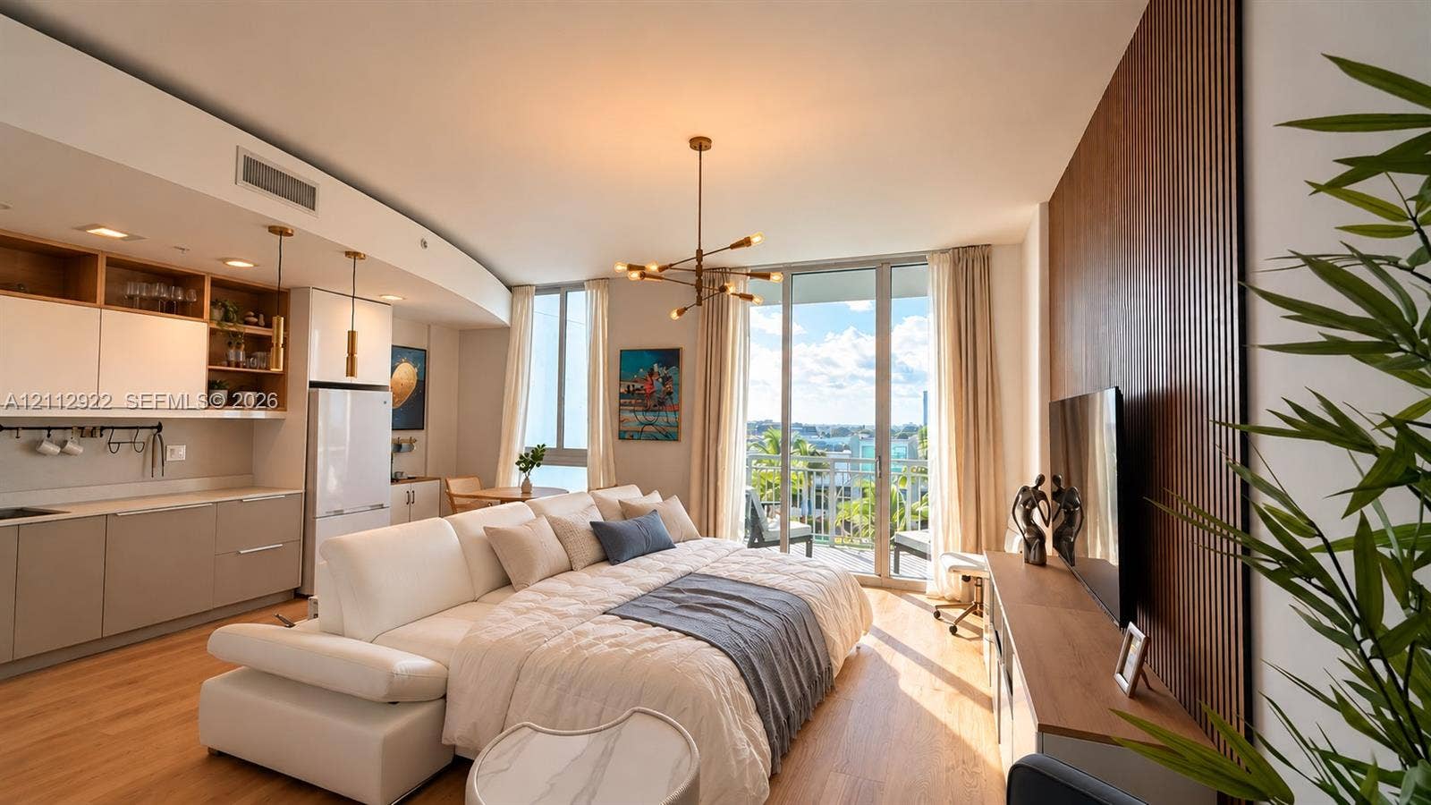 Open-concept interior featuring wood-finish flooring, floor-to-ceiling glass doors, built-in kitchen cabinetry with open shelving, vertical wood-slat accent wall, and a multi-arm brass chandelier