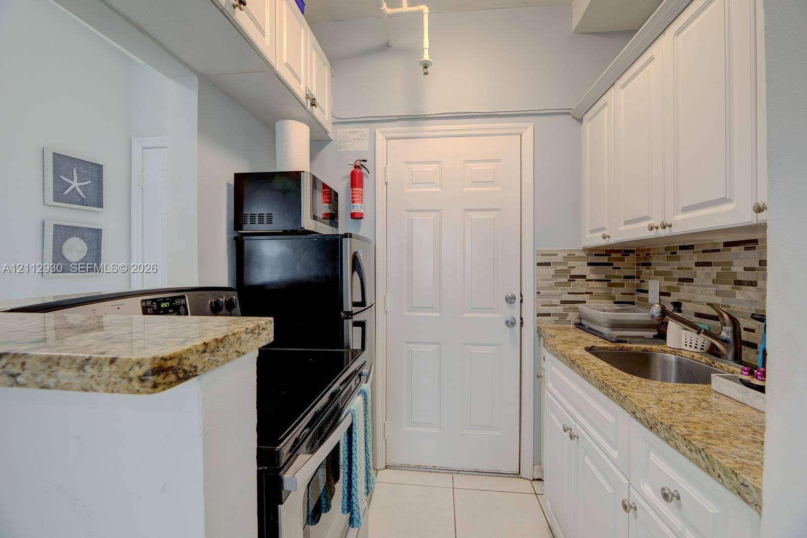 3030 Collins Avenue, #1G, Miami Beach, FL 33140 Kitchen featuring white cabinetry, stone-finish countertops, tile backsplash, stainless steel sink, and tile flooring