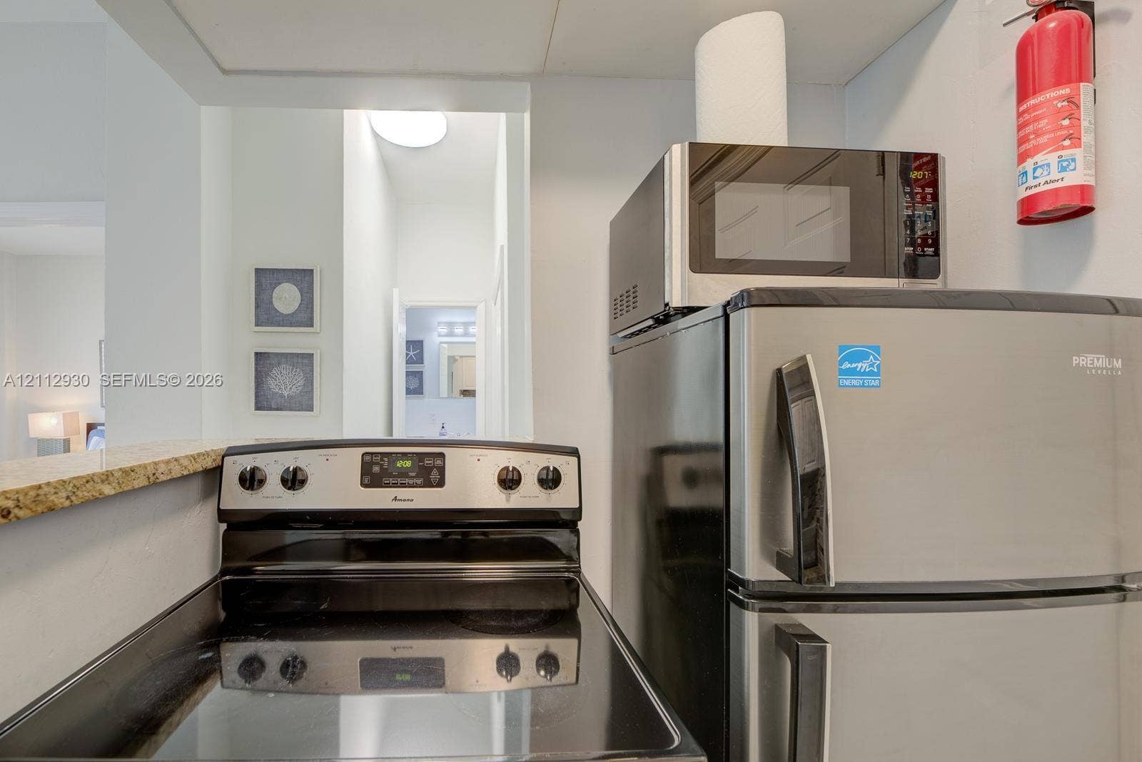 3030 Collins Avenue, #1G, Miami Beach, FL 33140 Stainless steel refrigerator, built-in microwave, and electric range with a glass cooktop, finished with a stone-surface pass-through counter