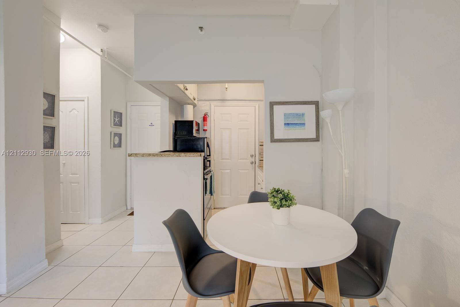 3030 Collins Avenue, #1G, Miami Beach, FL 33140 Kitchen featuring a breakfast bar with stone-surfaced countertop, white cabinetry, and ceramic tile flooring