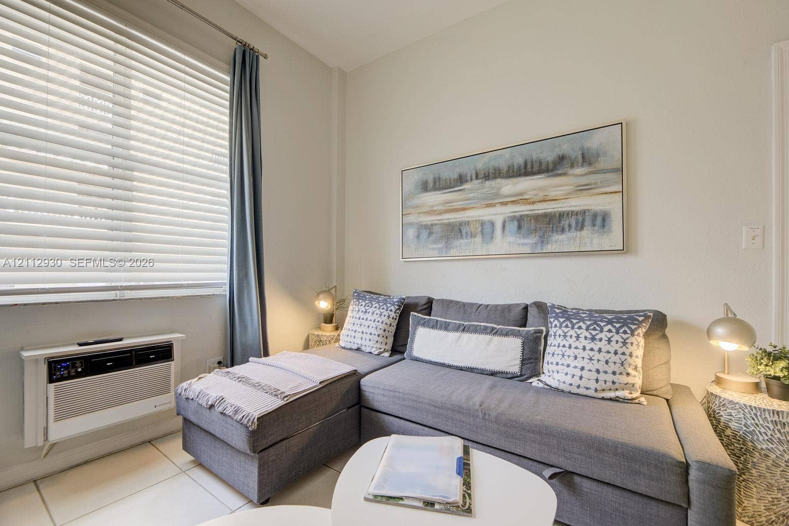 3030 Collins Avenue, #1G, Miami Beach, FL 33140 Neutral-toned interior featuring horizontal window blinds and a wall-mounted climate control unit