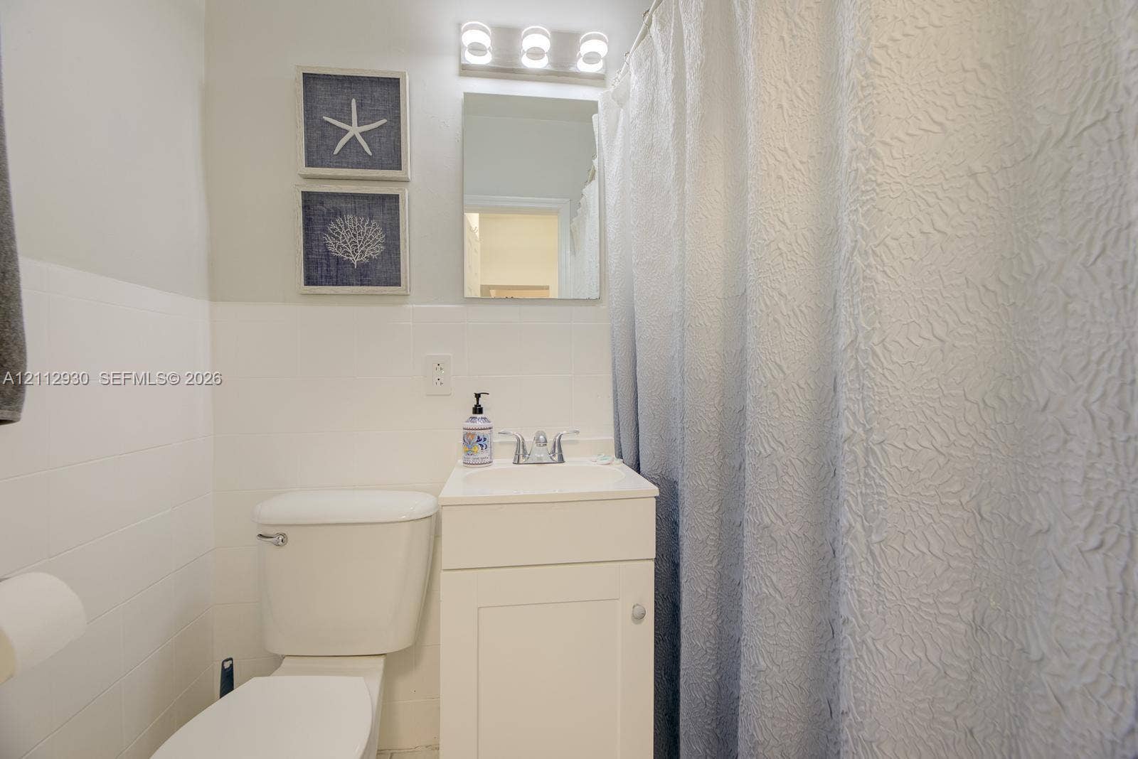 3030 Collins Avenue, #1G, Miami Beach, FL 33140 Bathroom featuring white cabinetry, a single-basin sink with a metallic faucet, a wall-mounted rectangular mirror, and a three-bulb light fixture