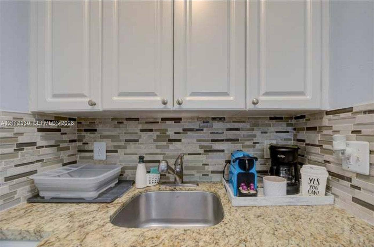 3030 Collins Avenue, #1G, Miami Beach, FL 33140 White cabinetry, stone-finish countertops, stainless steel undermount sink, gooseneck faucet, and multicolored linear glass tile backsplash