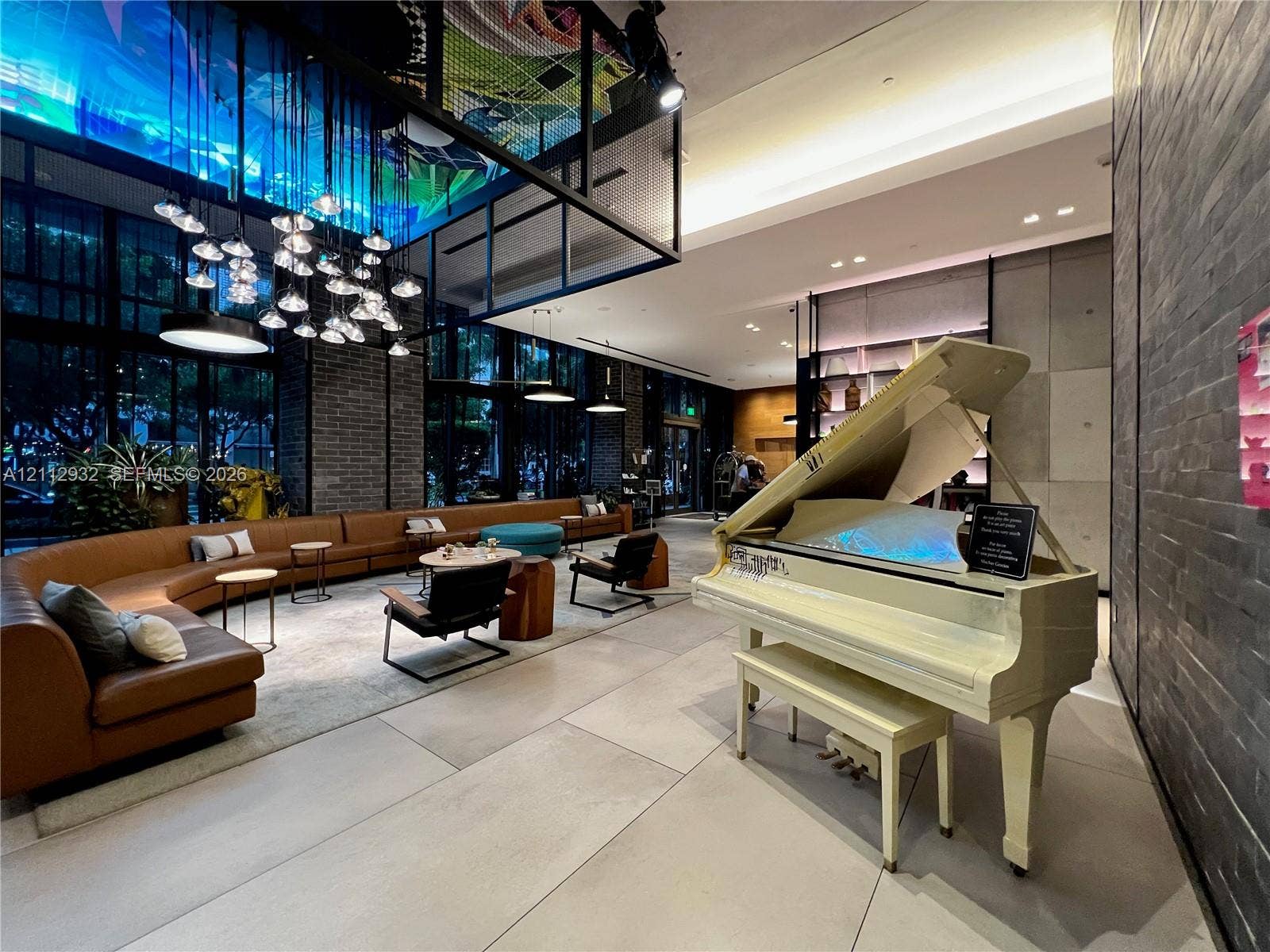 121 NE 34th Street, #903, Miami, FL 33137 Expansive lobby featuring large-format tile flooring, exposed dark brick walls, floor-to-ceiling windows, and a tiered multi-pendant lighting installation