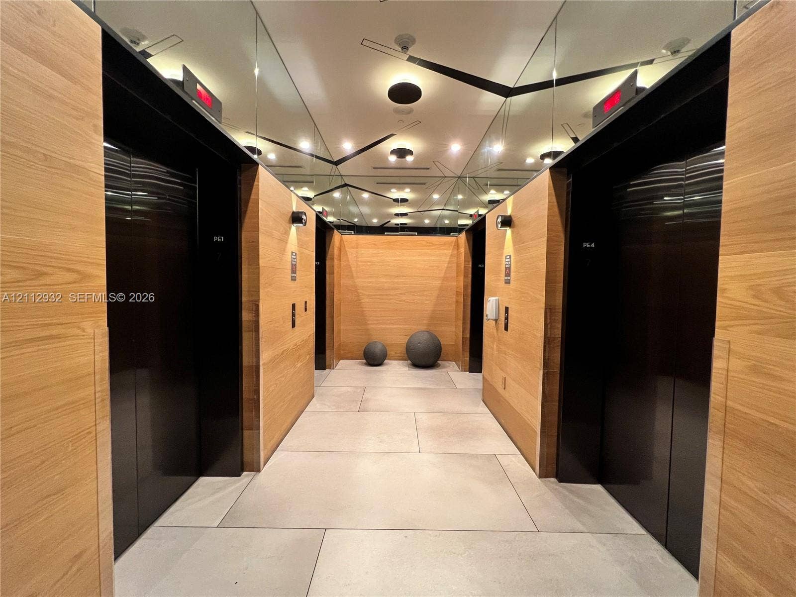 121 NE 34th Street, #903, Miami, FL 33137 Elevator lobby featuring wood-finish wall paneling, large-format tile flooring, mirrored ceiling panels, and high-contrast metal elevator doors
