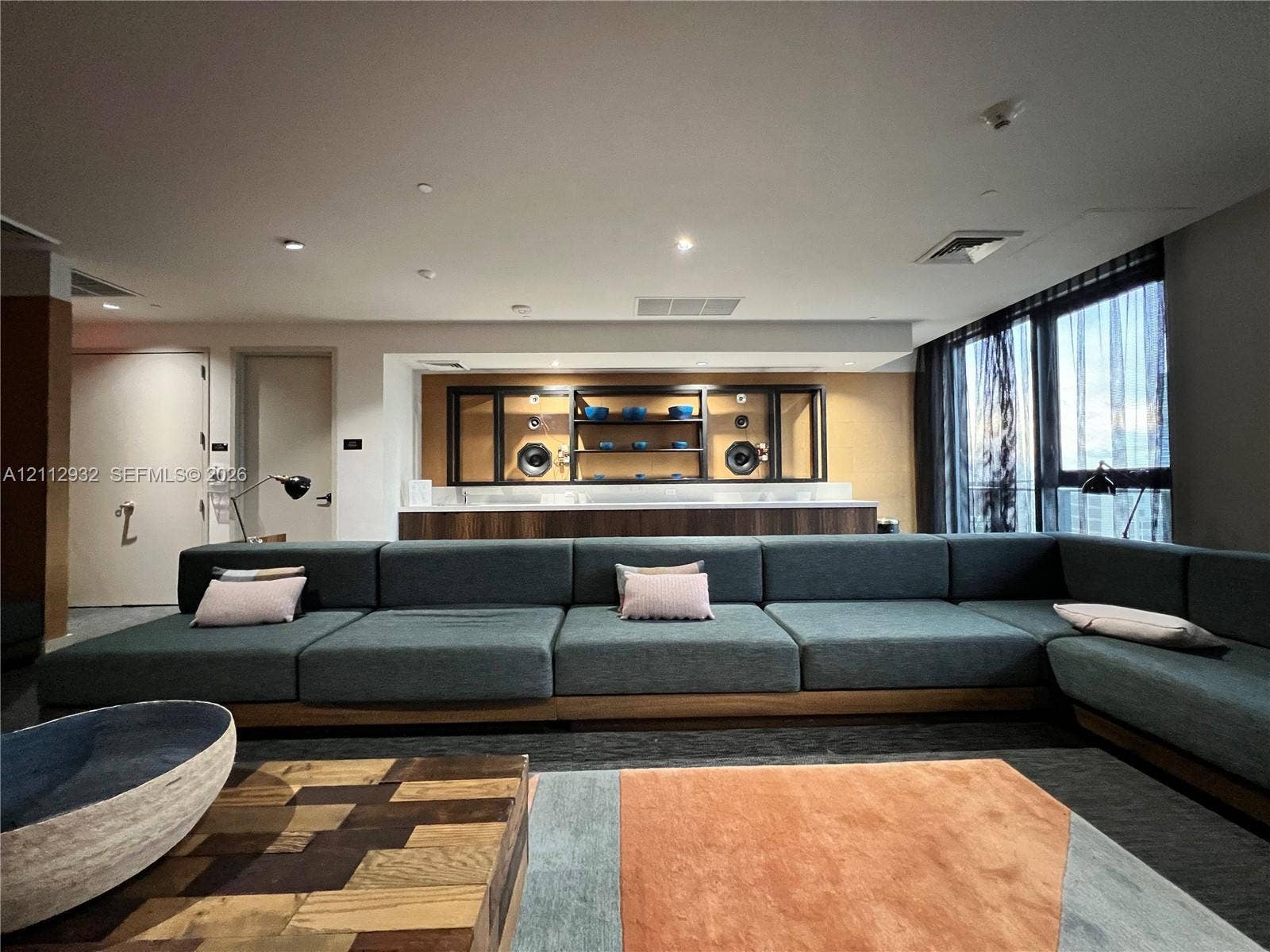 121 NE 34th Street, #903, Miami, FL 33137 Built-in media console with wood-finish cabinetry, quartz countertop, and integrated shelving, featuring floor-to-ceiling windows with expansive glass panels and recessed ceiling lighting