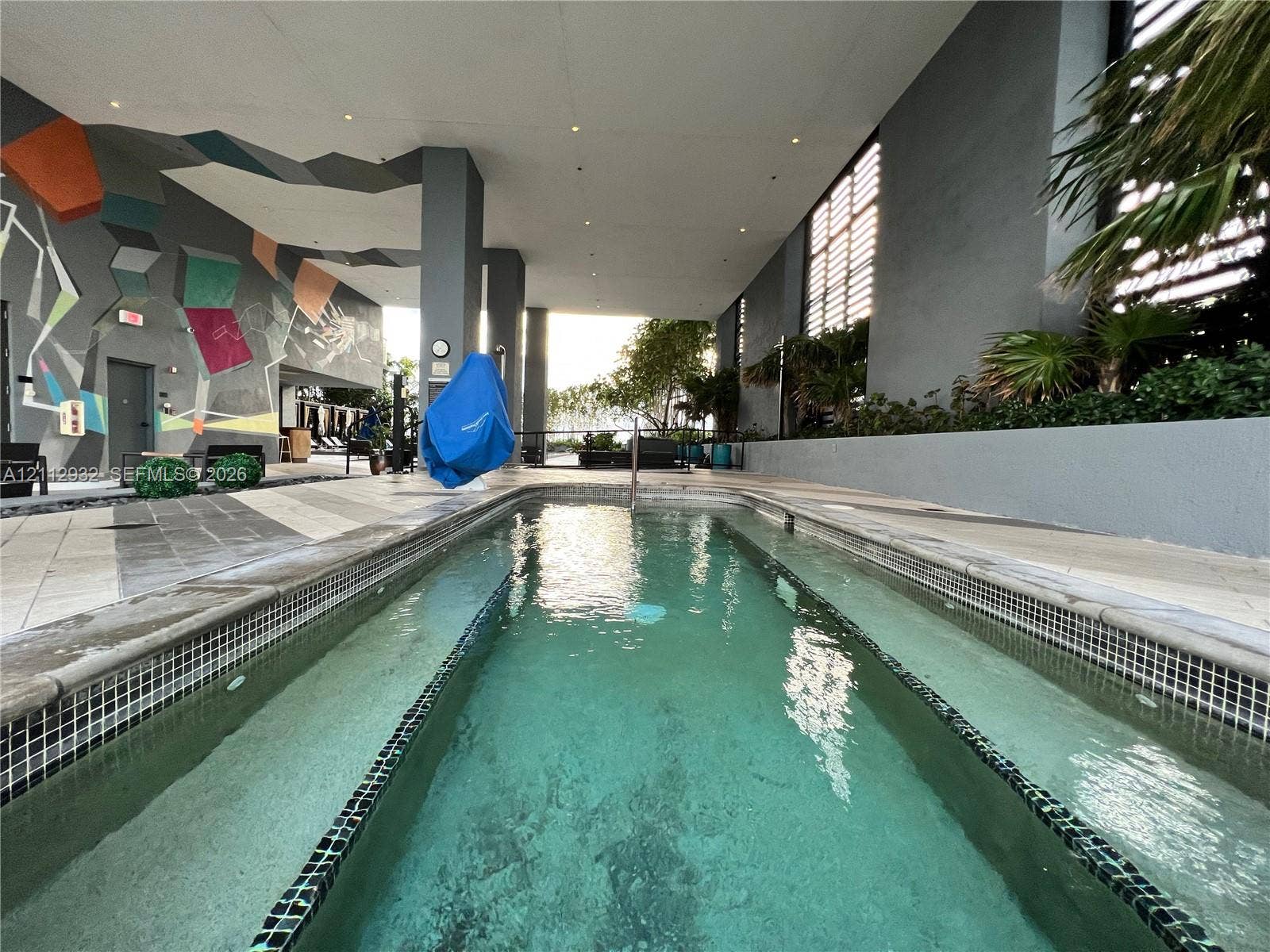 121 NE 34th Street, #903, Miami, FL 33137 Covered swimming pool featuring tiled coping, geometric mural wall, recessed ceiling lighting, and large-format tile decking