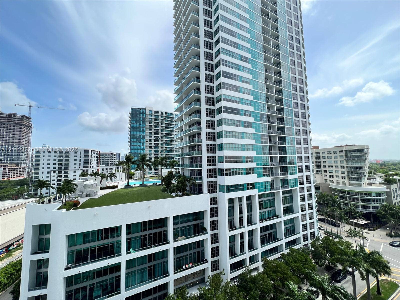 121 NE 34th Street, #903, Miami, FL 33137 High-rise glass and concrete tower featuring tiered balcony levels, a landscaped elevated terrace, and ground-level palm tree accents