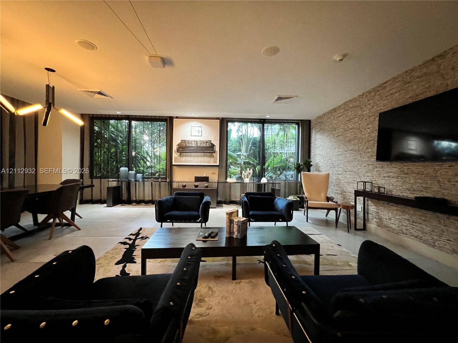 121 NE 34th Street, #903, Miami, FL 33137 Living area featuring large-format tile flooring, textured stone accent wall, multi-panel sliding glass doors, contemporary geometric chandelier, and recessed ceiling lighting