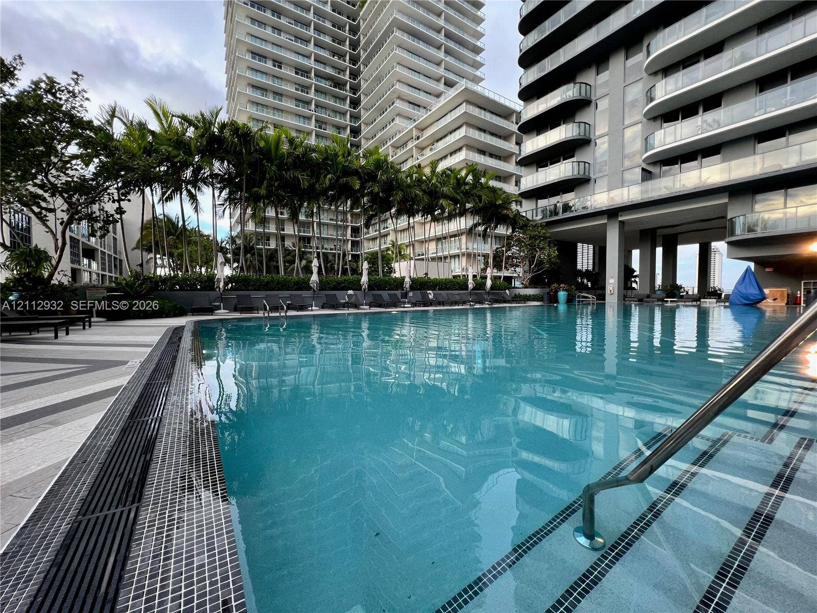 121 NE 34th Street, #903, Miami, FL 33137 Swimming pool featuring a tiled perimeter, metal handrails, a paved deck, and surrounding palm trees
