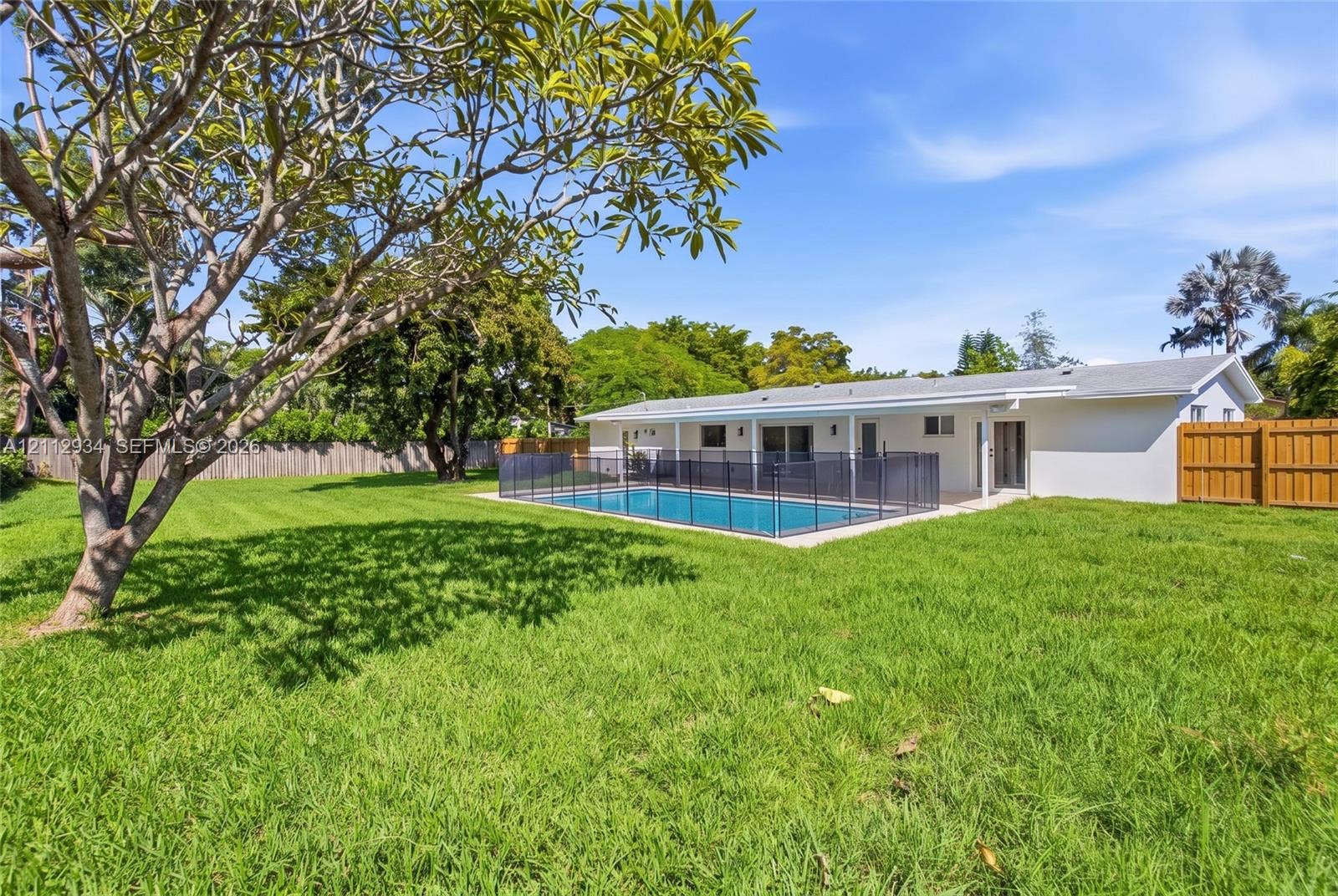 14620 SW 83rd Avenue, Palmetto Bay, Palmetto Bay, FL 33158 Spacious backyard featuring a grass lawn, mature trees, a swimming pool with a perimeter safety fence, a covered patio, and wood-style privacy fencing