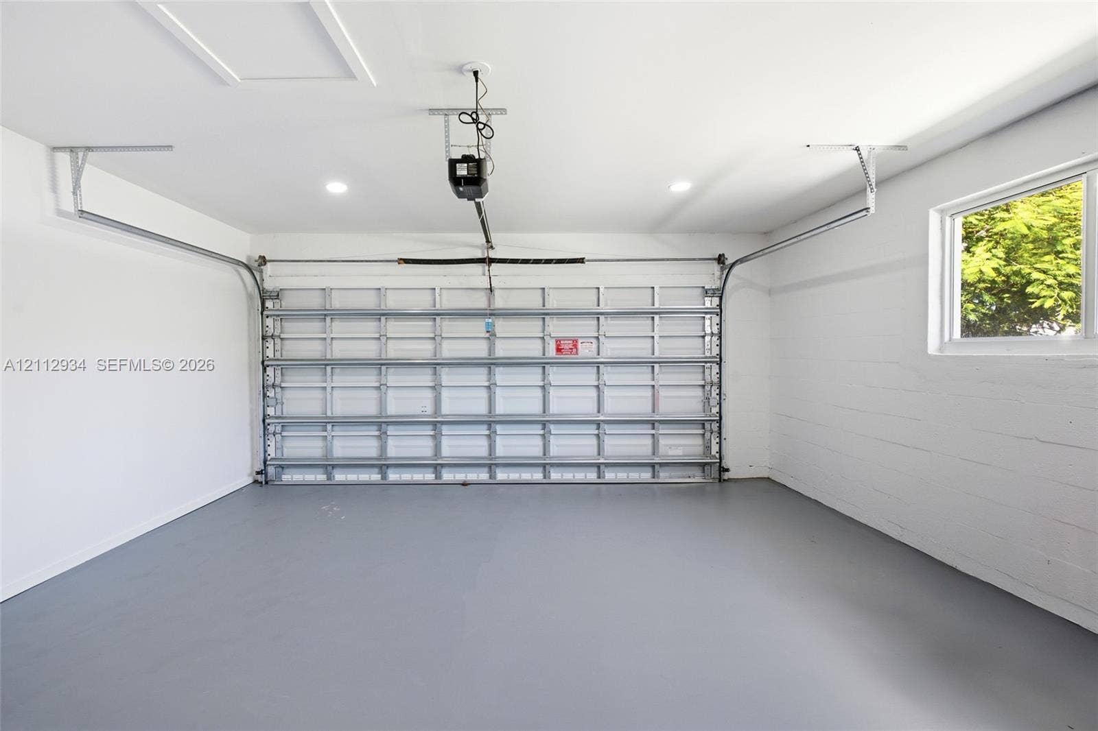 14620 SW 83rd Avenue, Palmetto Bay, Palmetto Bay, FL 33158 Finished garage featuring white-painted masonry walls, a grey-toned sealed concrete floor, recessed ceiling lighting, and a window providing natural light