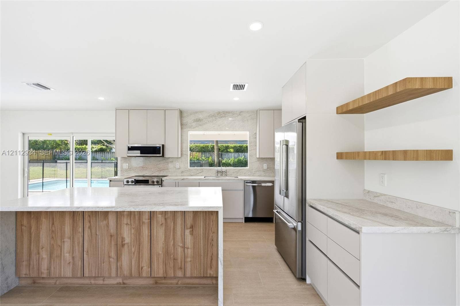 14620 SW 83rd Avenue, Palmetto Bay, Palmetto Bay, FL 33158 Kitchen featuring a wood-tone island with waterfall stone countertop, neutral flat-panel cabinetry, stone backsplash, built-in stainless steel appliances, and floating wood shelving