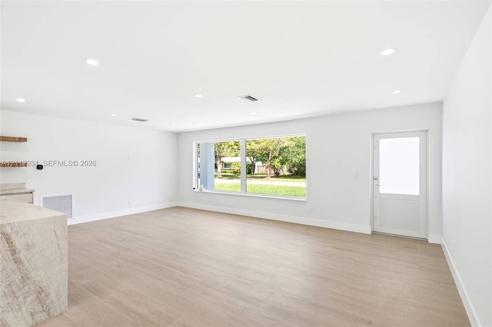 14620 SW 83rd Avenue, Palmetto Bay, Palmetto Bay, FL 33158 Open-concept space featuring wood-finish flooring, recessed lighting, expansive picture window, natural stone-topped built-in cabinetry, and a glass-paneled exterior door