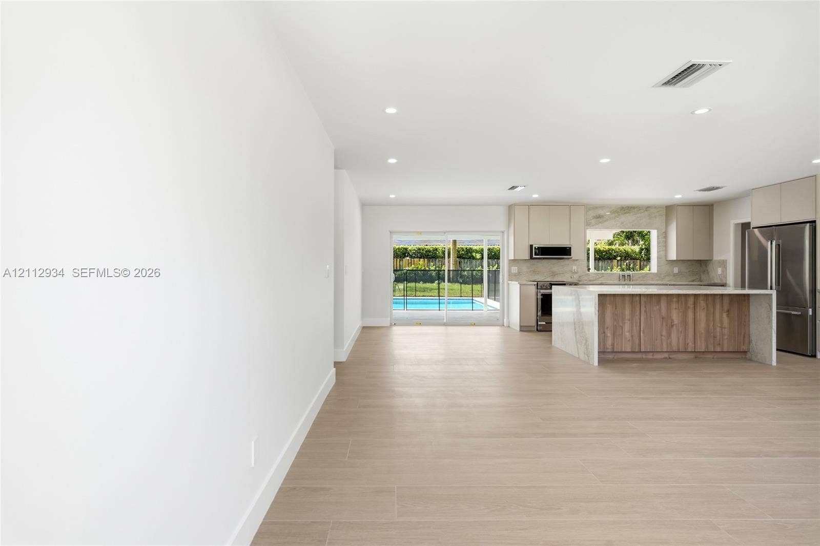 14620 SW 83rd Avenue, Palmetto Bay, Palmetto Bay, FL 33158 Open-concept kitchen featuring an island with a waterfall-edge stone countertop, wood-finish cabinetry, recessed lighting, and wood-finish flooring, with sliding glass doors leading to a pool area