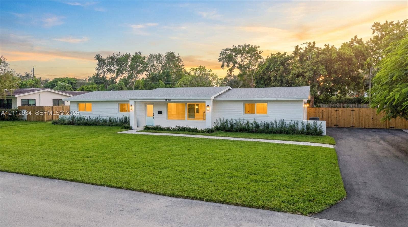 14620 SW 83rd Avenue, Palmetto Bay, Palmetto Bay, FL 33158 Single-story residence featuring a white horizontal siding exterior, low-pitch roof, concrete walkway, expansive front lawn, and paved side driveway