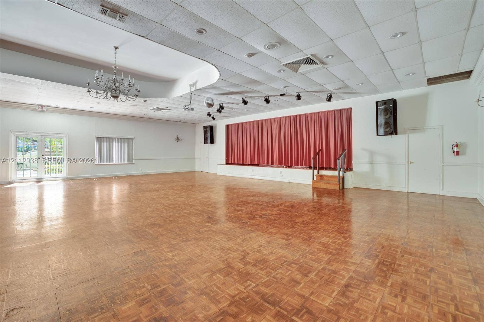 3800 S Ocean Drive, #801, Hollywood, FL 33019 Expansive open-concept space featuring parquet wood-finish flooring, a raised stage with a curtained backdrop, drop ceiling with recessed lighting, a decorative chandelier, and double glass-panel doors