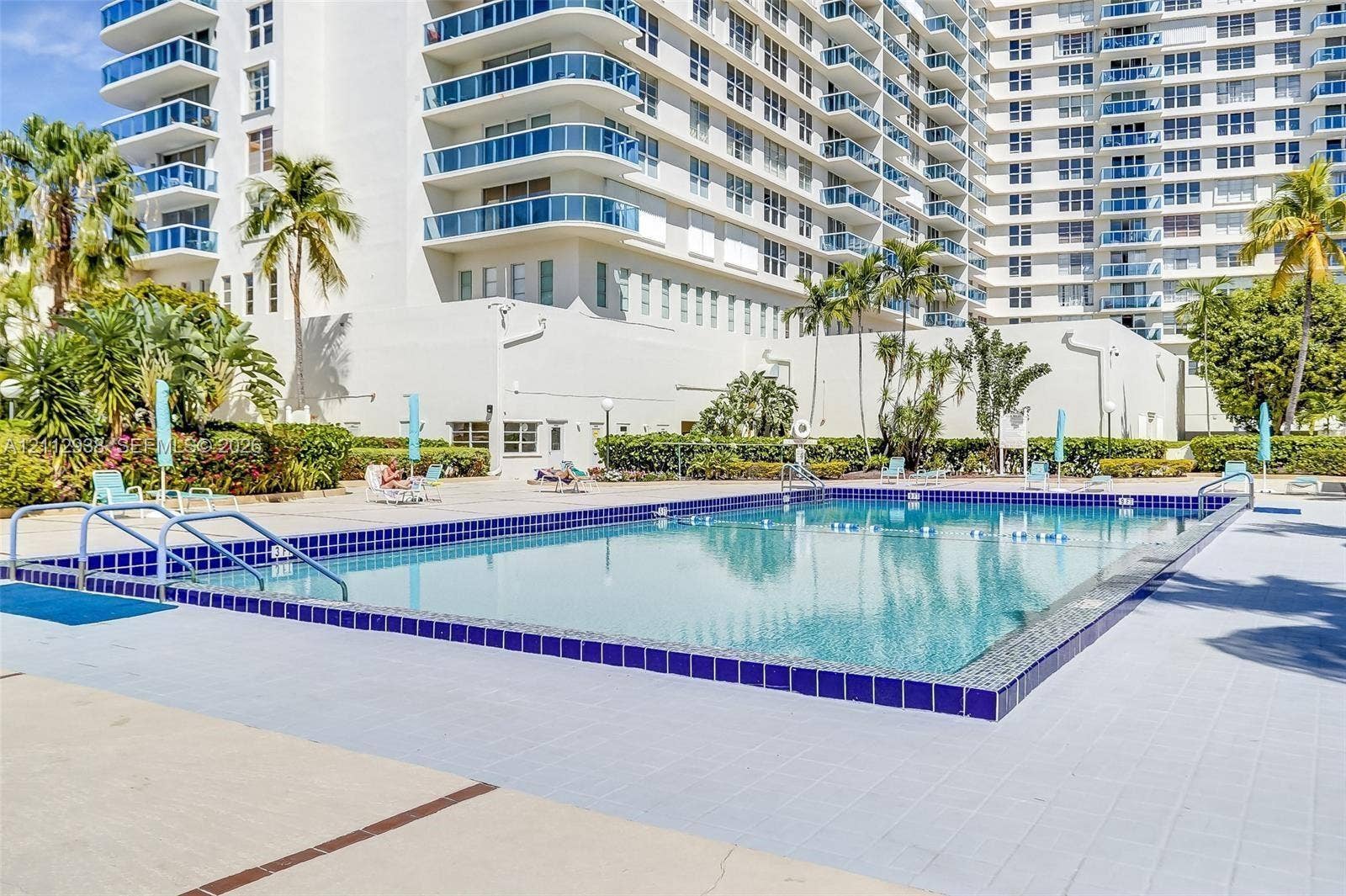 3800 S Ocean Drive, #801, Hollywood, FL 33019 In-ground swimming pool with a tiled perimeter, surrounded by a paved deck, mature palm trees, and professional landscaping