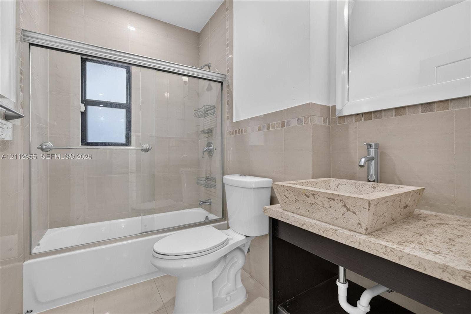 549 NE 12th Avenue, Fort Lauderdale, FL 33301 Bathroom featuring a custom stone vessel sink with a chrome faucet, solid-surface vanity countertop, glass-enclosed shower with tiled walls, and decorative accent tiling